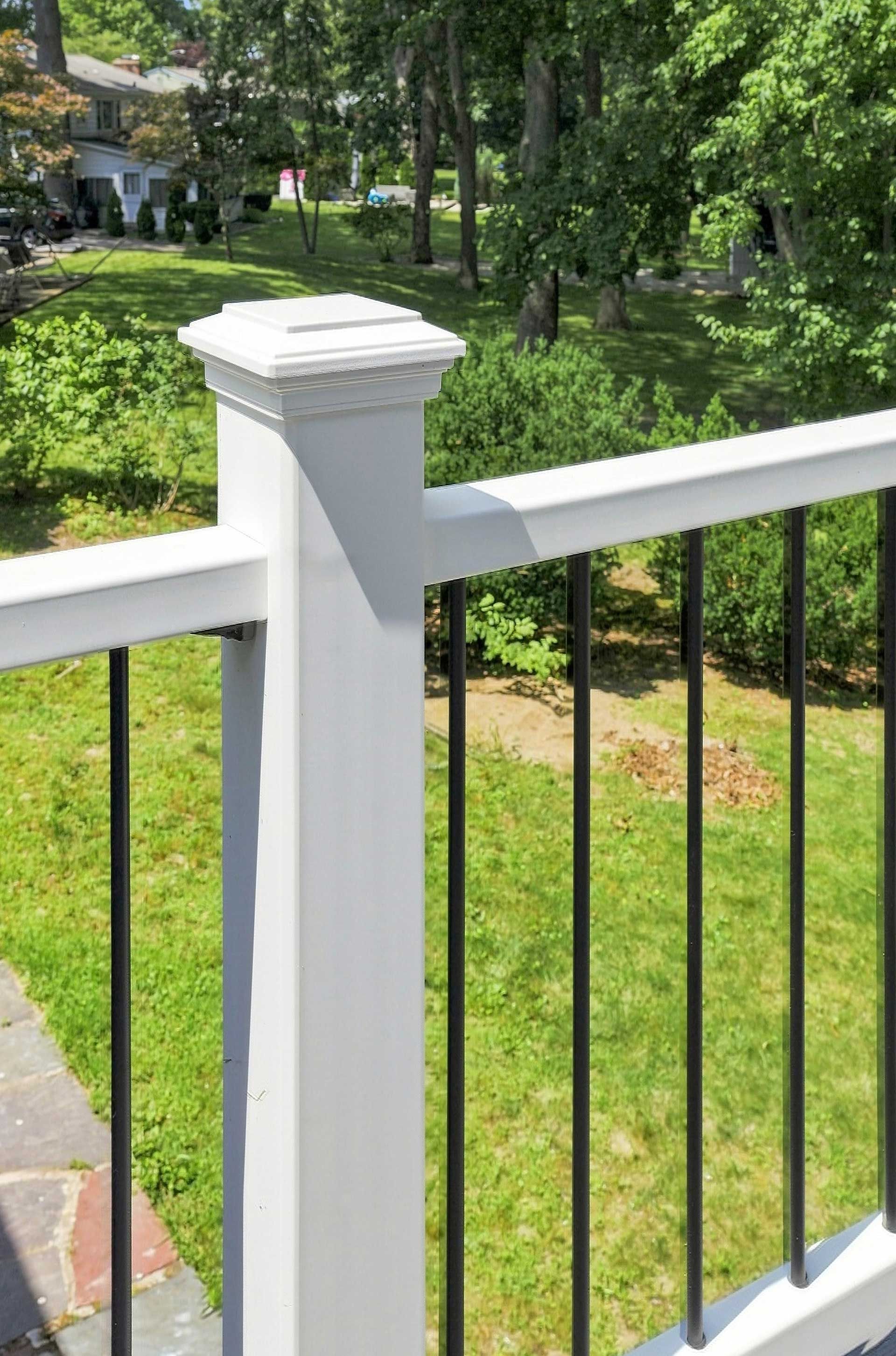 White deck railing with black balusters overlooking a green front yard and trees