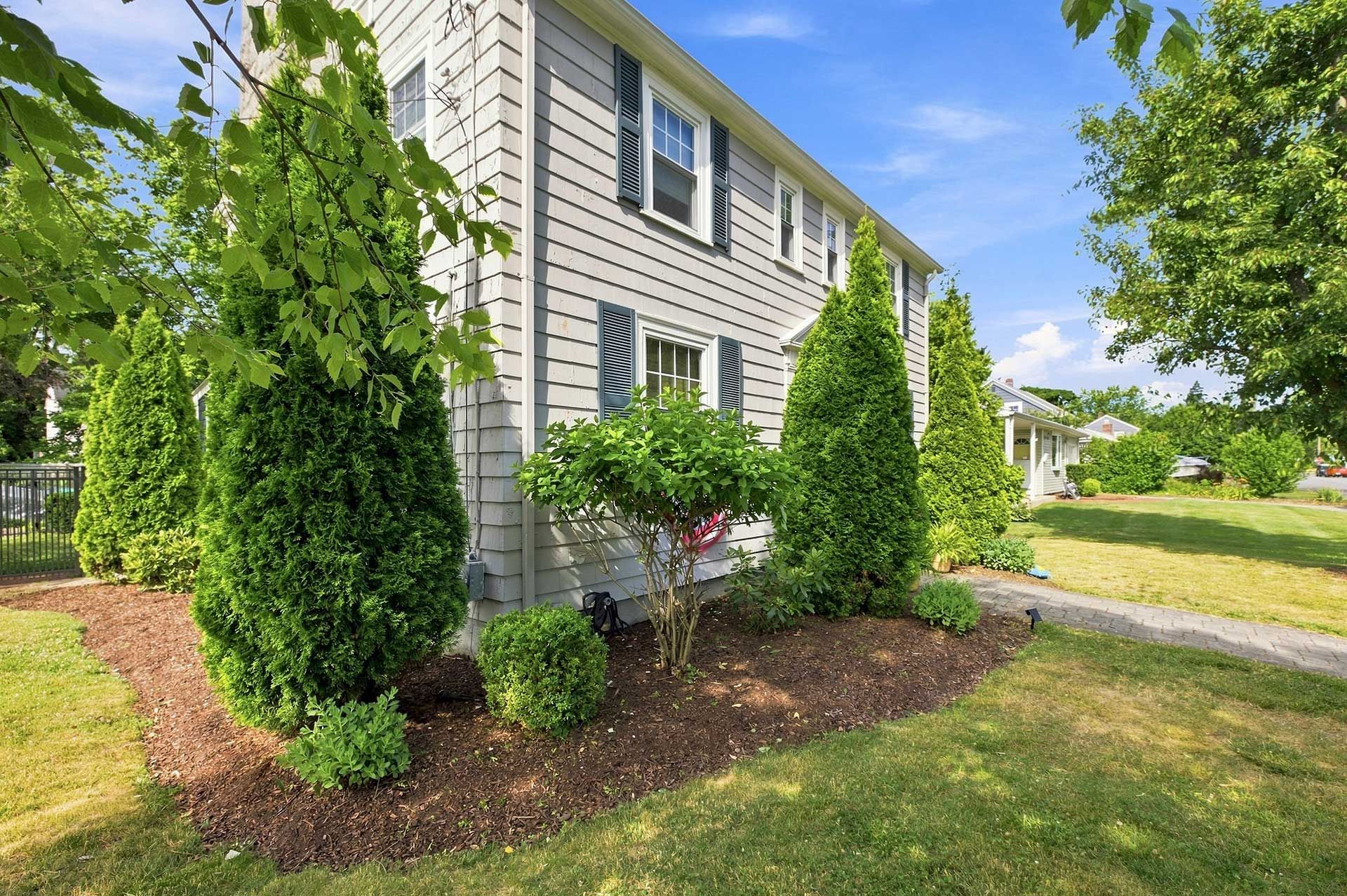 Suburban house exterior with gray siding, white trim, green shrubs, and a sunny lawn