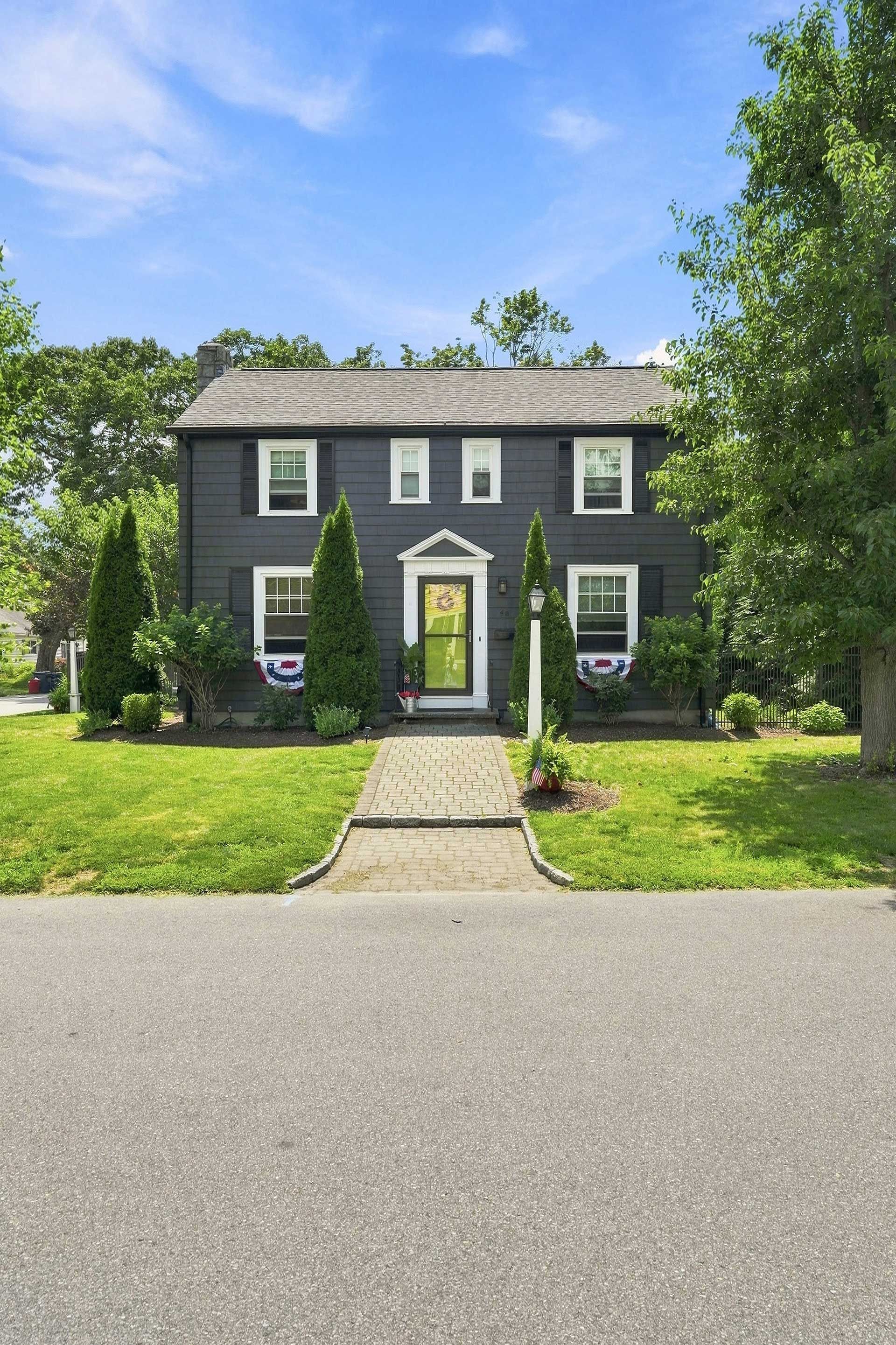 Two-story dark gray house with white trim, central door, and front lawn under a blue sky