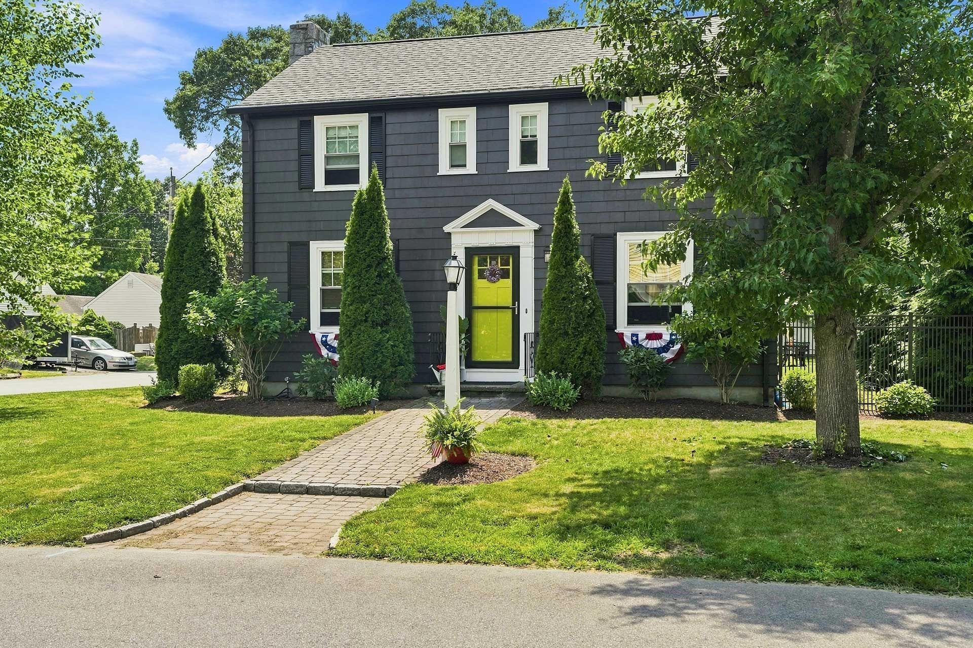 Dark gray house with bright green door, front walkway, and green lawn under trees