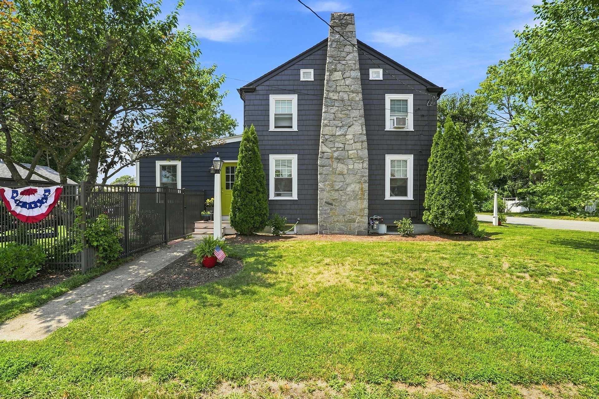 Dark gray stone house with white-trimmed windows, green lawn, and trees in front