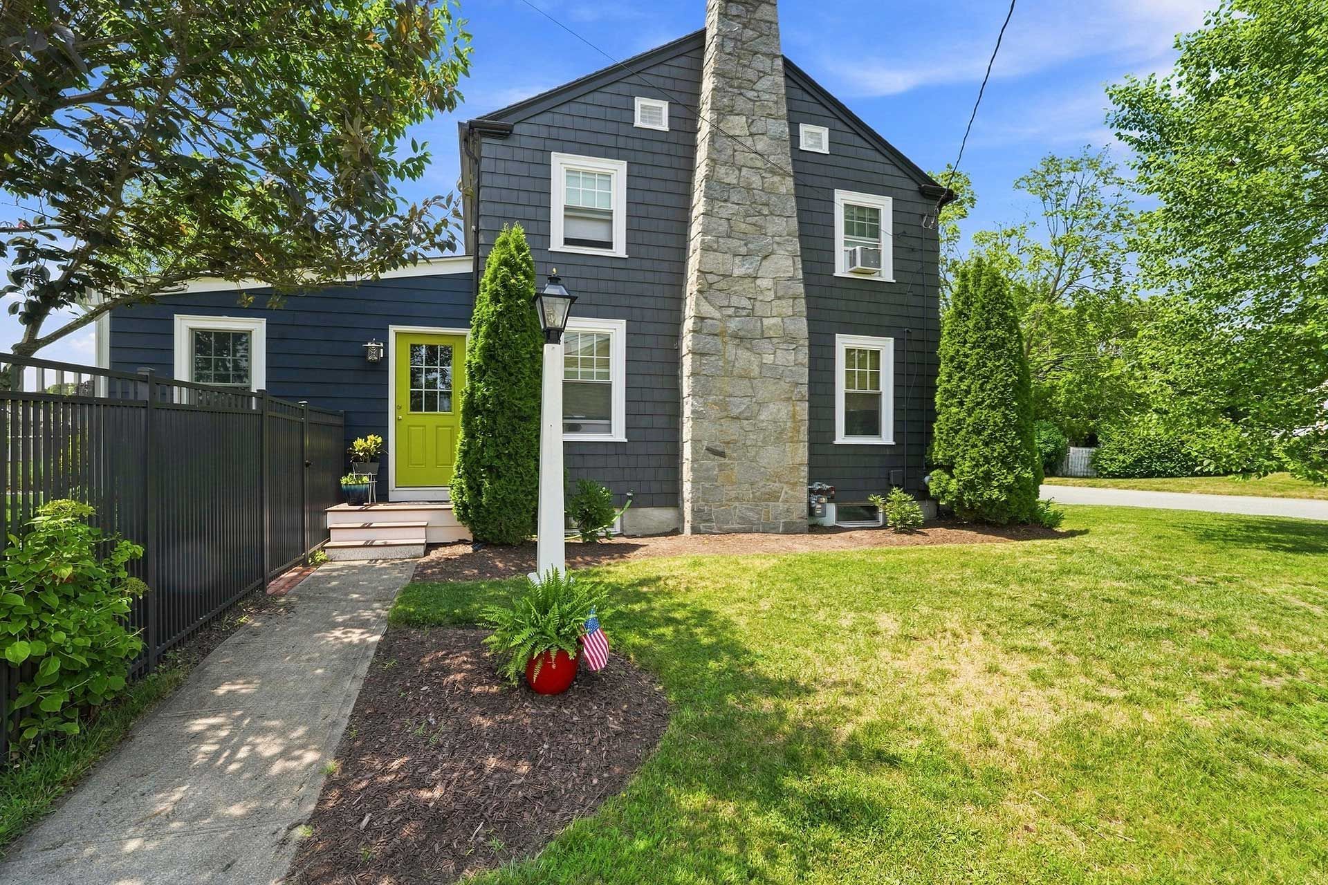 Dark blue and gray two-story house with bright green front door, black fence, and landscaped yard on a sunny day
