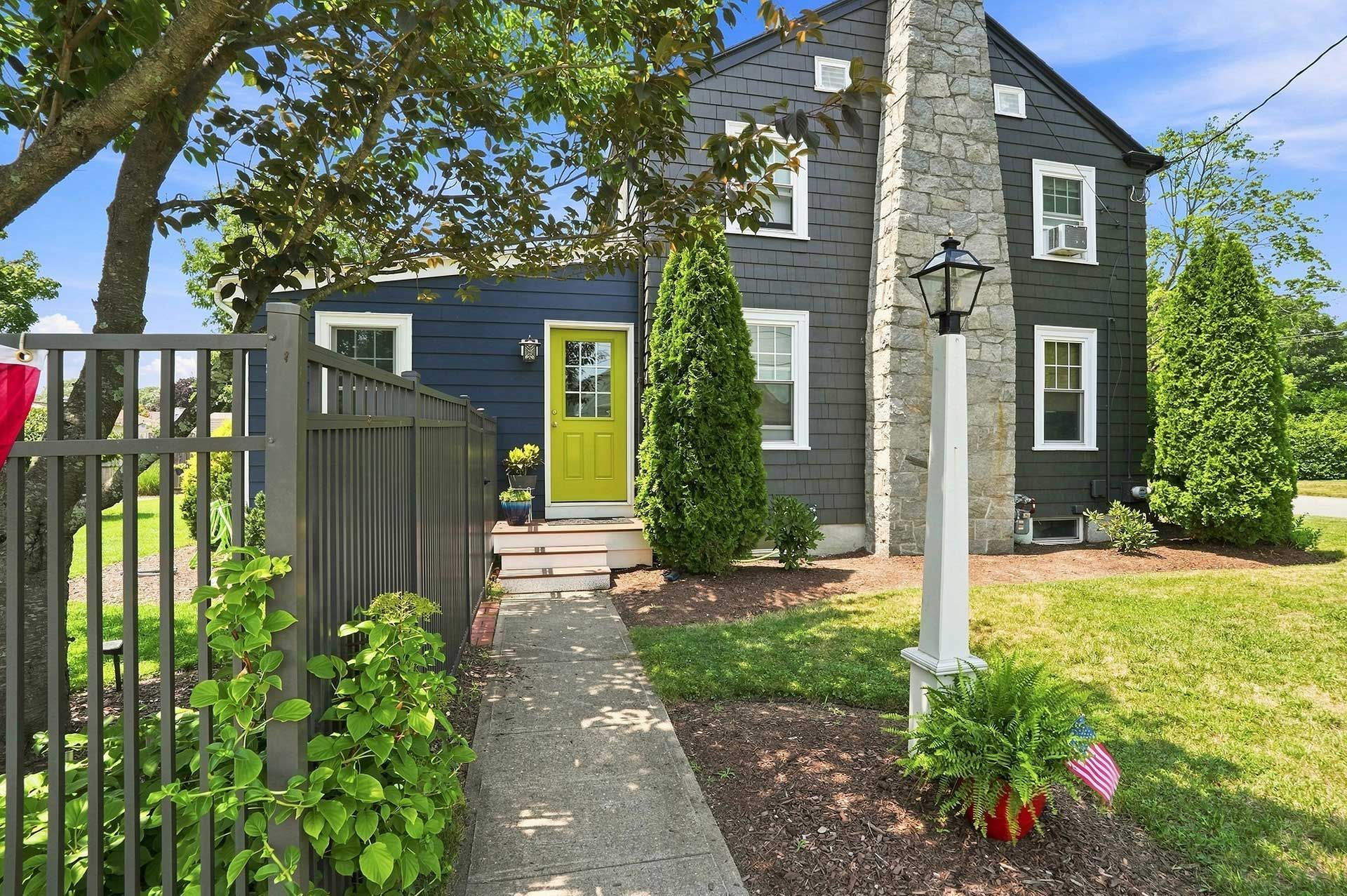 Dark gray house with bright green door, stone walkway, and front garden behind a fence