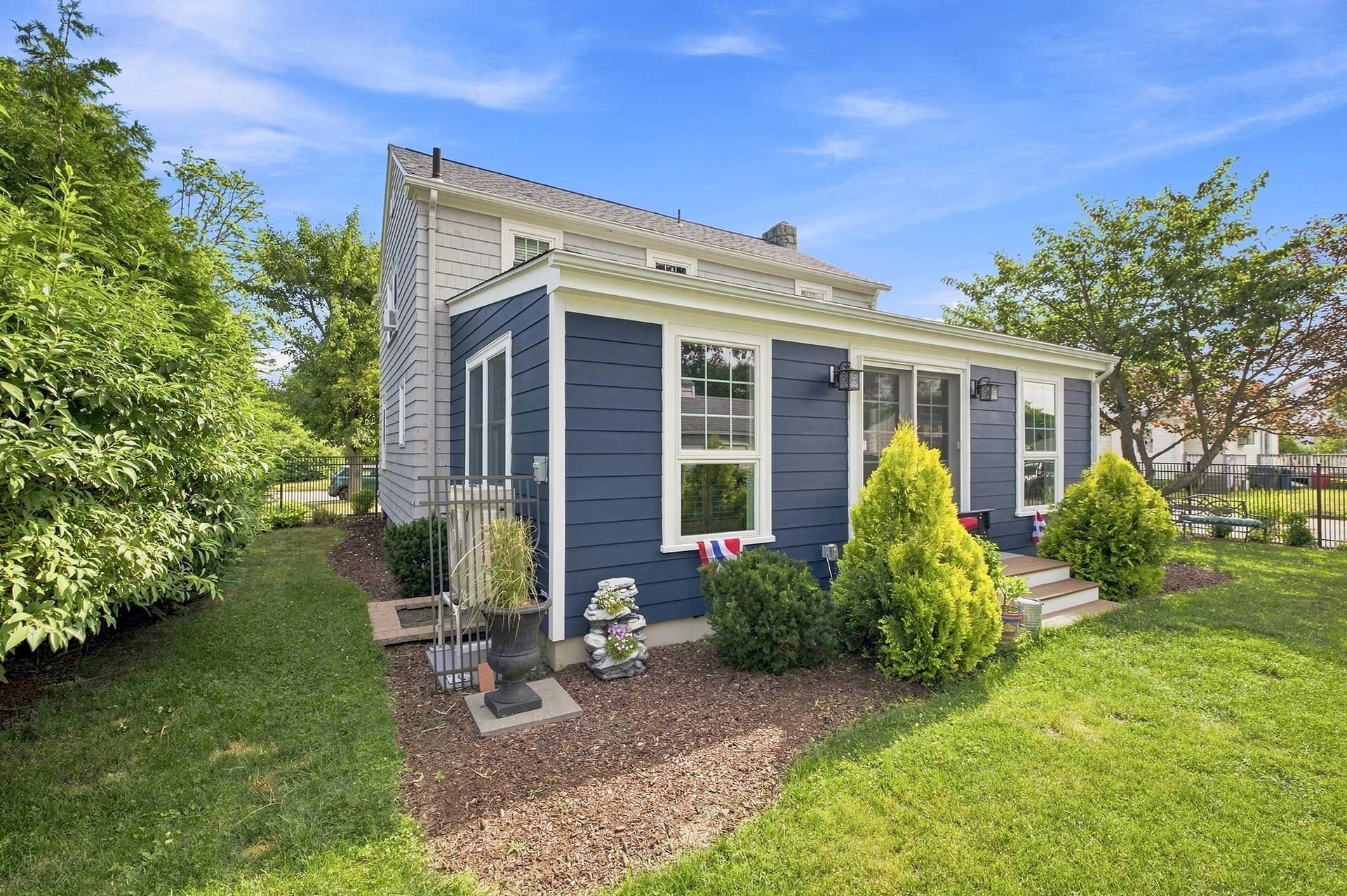 Small blue house with white trim, front garden, and lawn in a sunny yard