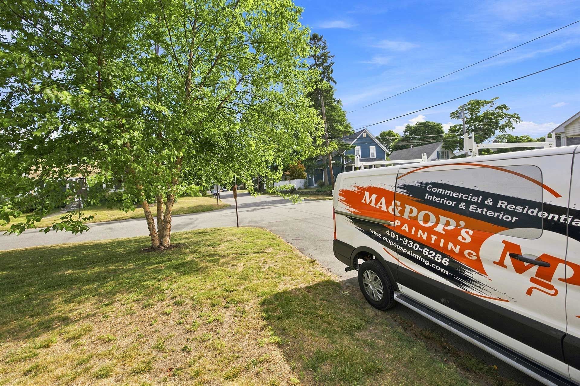 White service van with orange logo parked by a leafy suburban street on a sunny day
