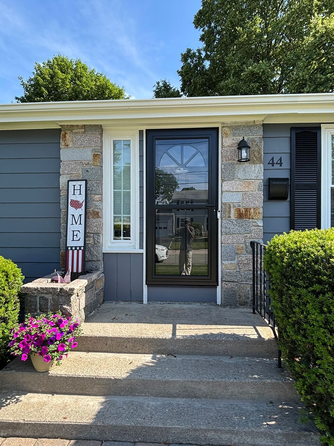 House front with stone facade, gray siding, black door. Steps lead to the entrance. 
