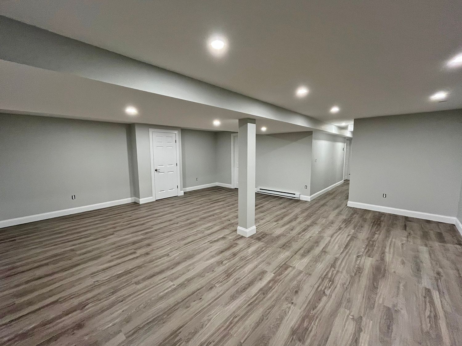 Finished basement with gray walls, wood-look flooring, recessed lighting, and a support beam.
