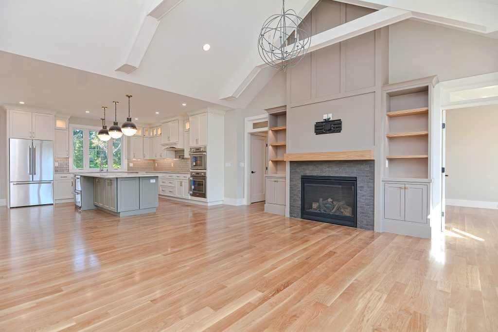 Spacious, open-concept home interior with light wood floors, fireplace, and kitchen visible in the background.