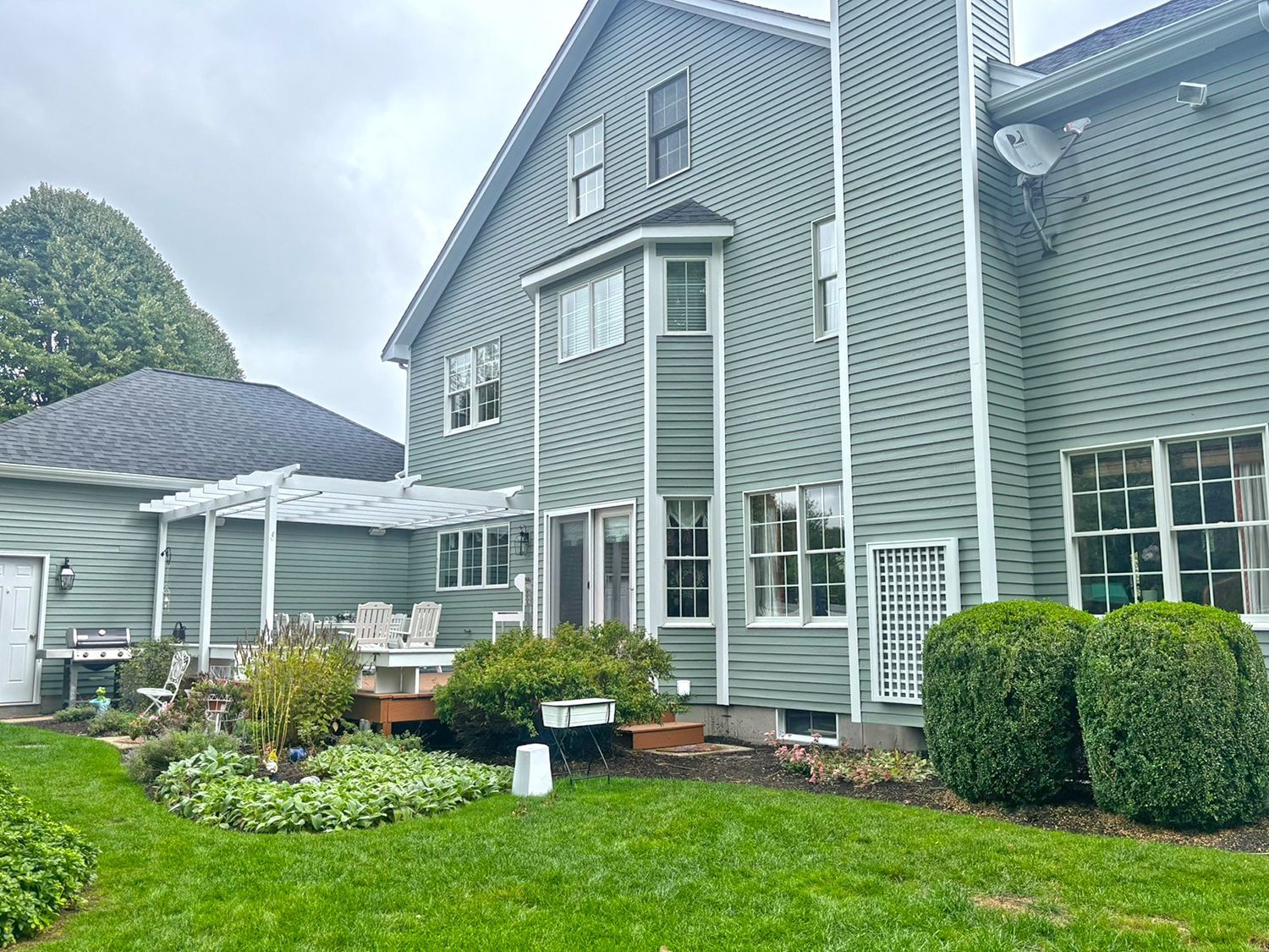 Green house exterior with bay window, deck, and pergola, on a cloudy day.