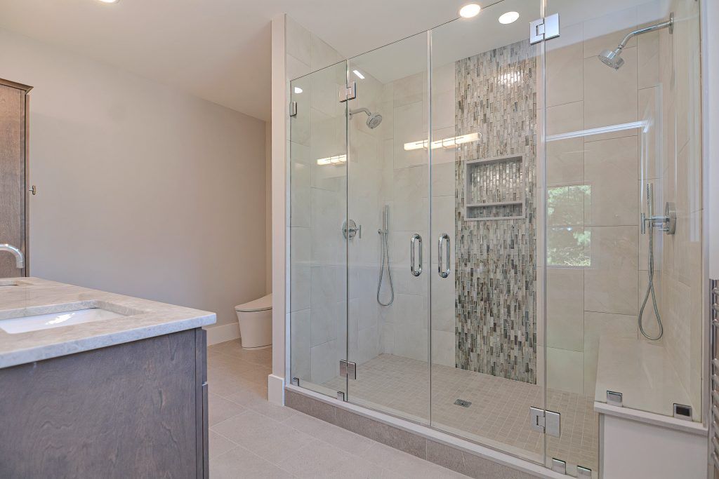 Bathroom with a large, glass-enclosed shower, featuring a mosaic accent wall and two shower heads.