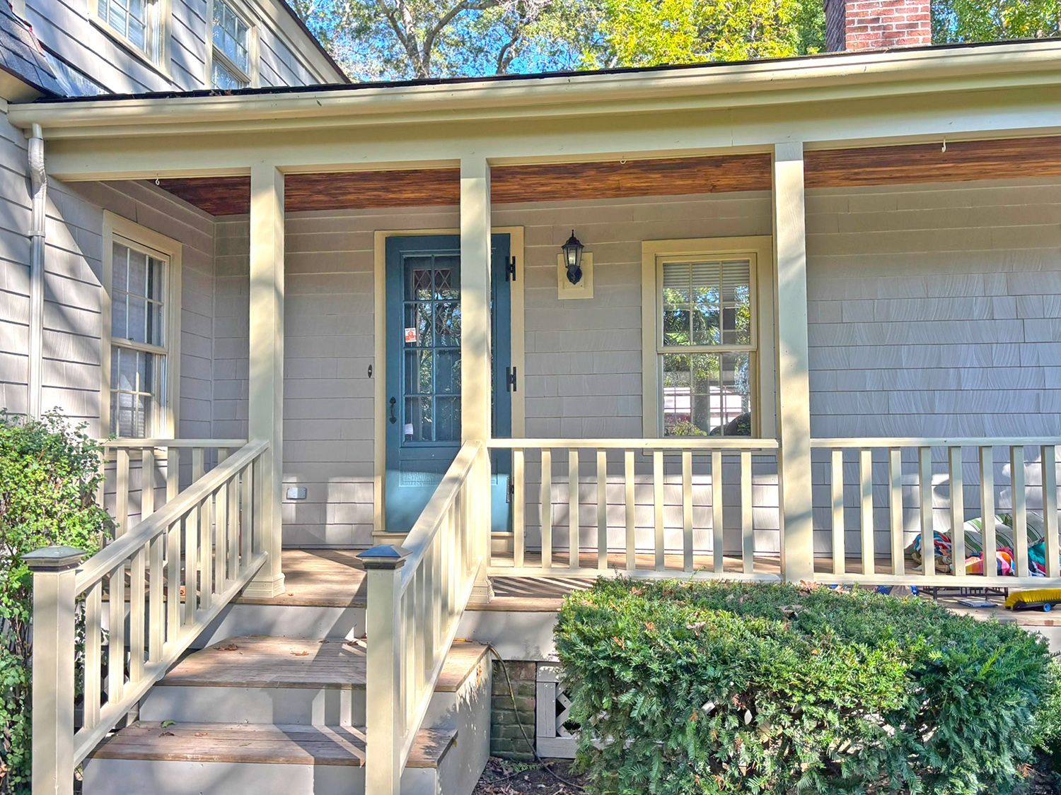 Porch of a light-colored house with stairs, railing, and a teal front door. Sunny day.