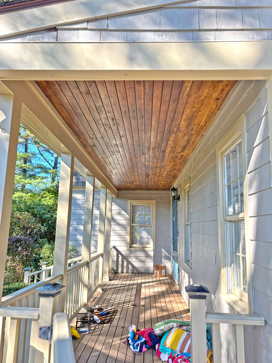 Covered porch with wood ceiling and floor; house exterior with windows.