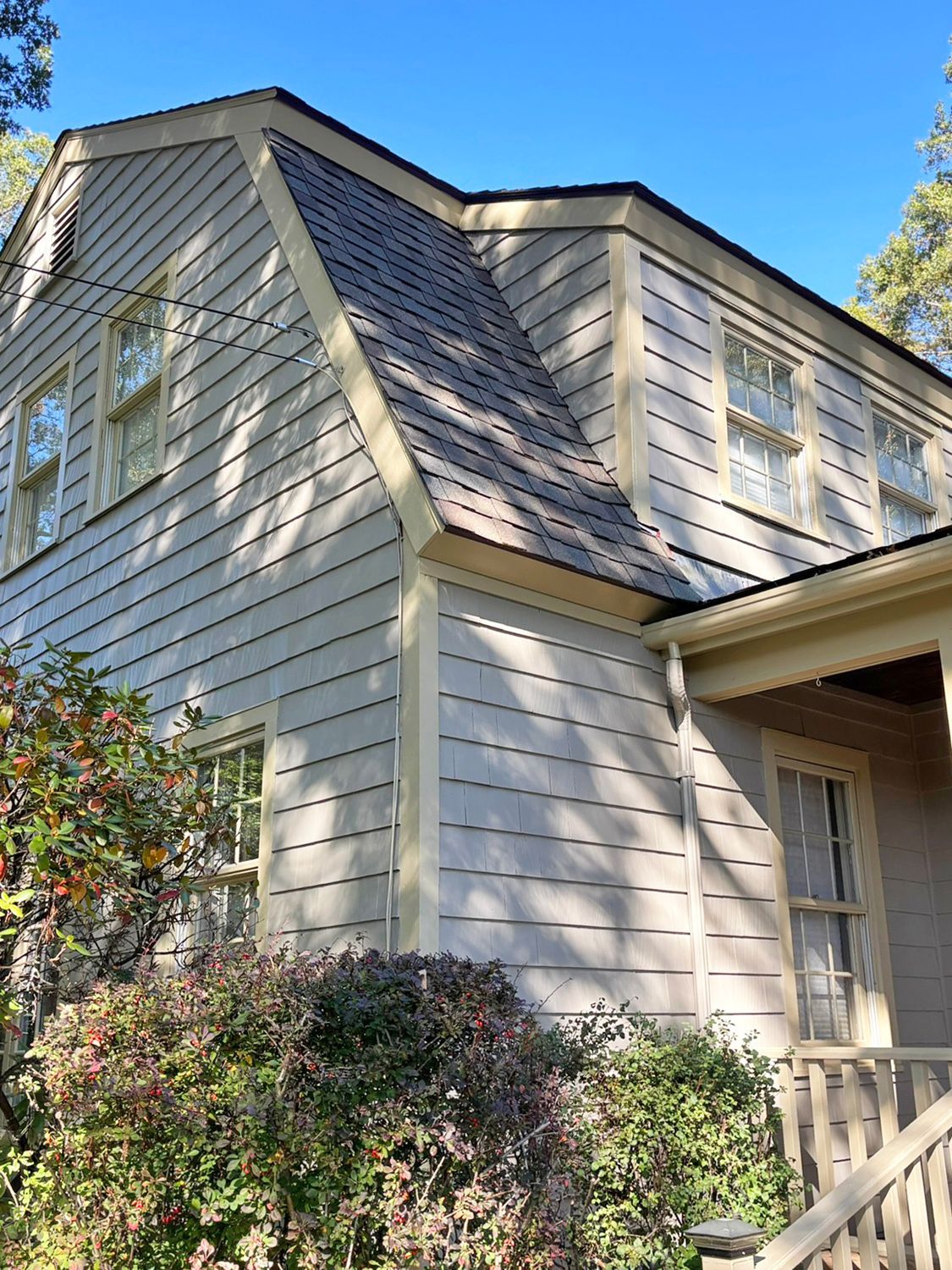 Beige house with a dark roof and multiple windows. The trim is light yellow, and the sky is blue.