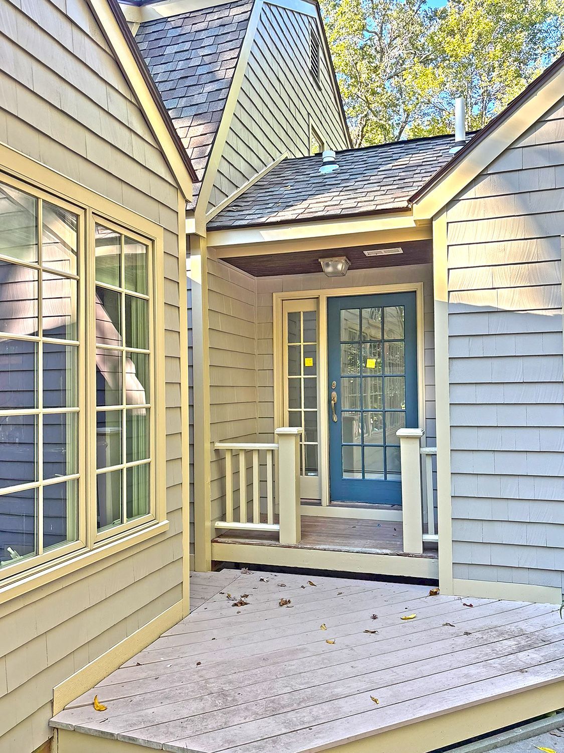 Exterior of a house with a teal door, covered porch, and light yellow siding; wooden deck.