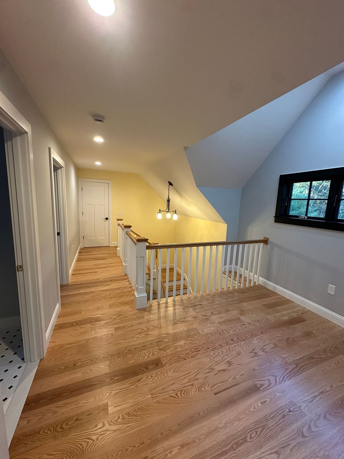 Wooden-floored hallway with a staircase, doors, and a light fixture, painted in gray, white, and yellow.