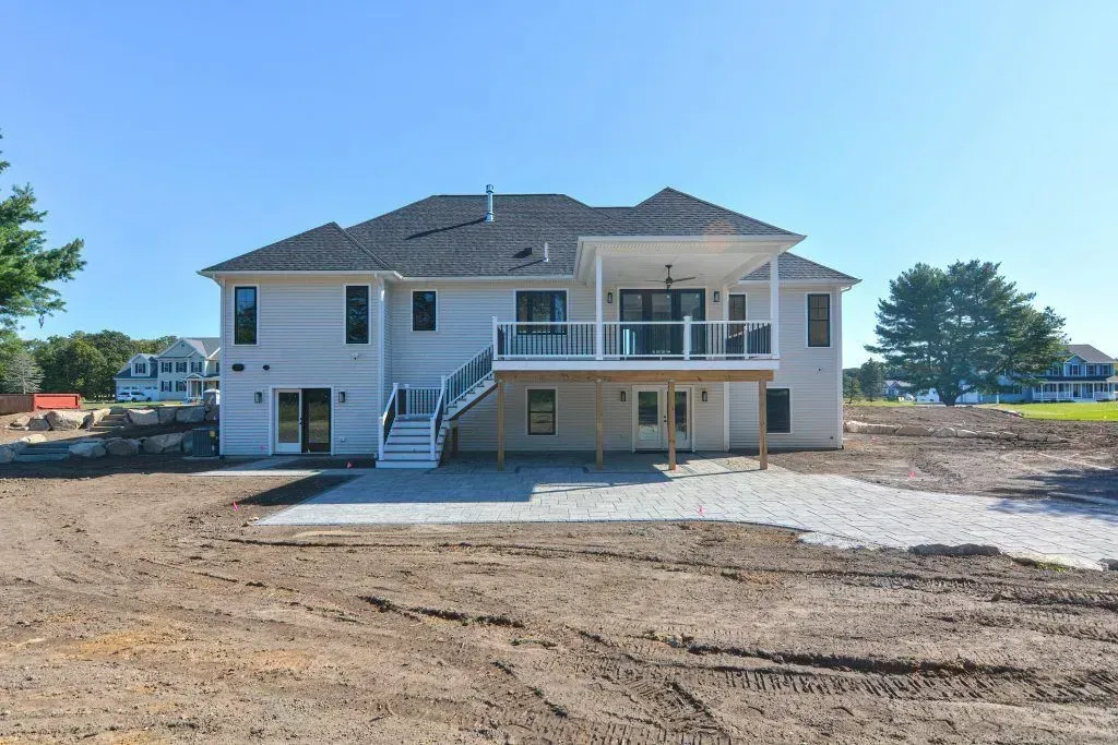 Rear view of a light-colored two-story house with a deck and stairs on a sunny day.