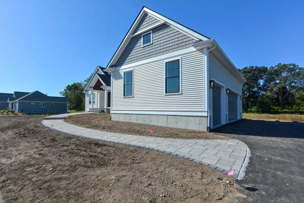 New house exterior with a paved walkway, garage, and blue sky.