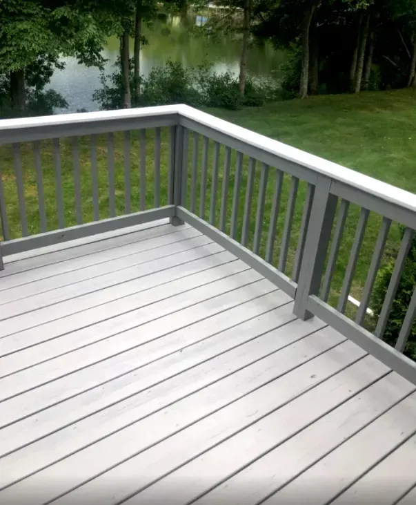 Gray wooden deck with railing overlooking a green lawn and lake.