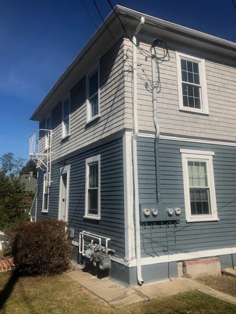 Two-story house with blue and gray siding, white trim, and a fire escape on the side, under a clear blue sky.