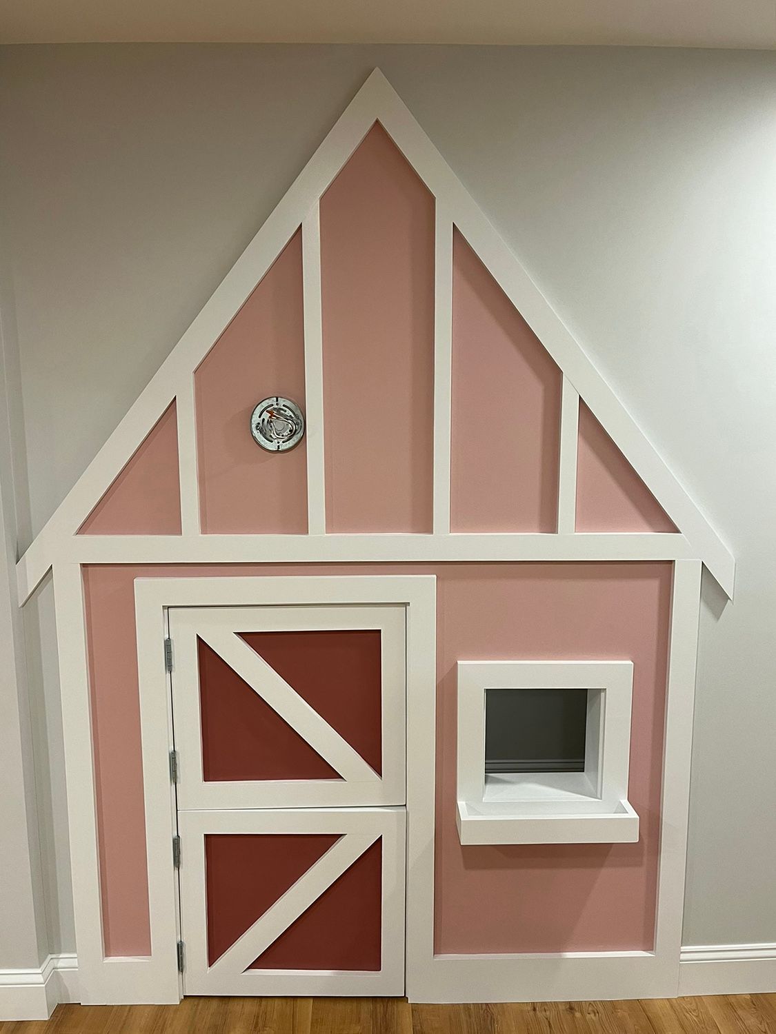 Pink playhouse built into a wall, with white trim, door, and window.