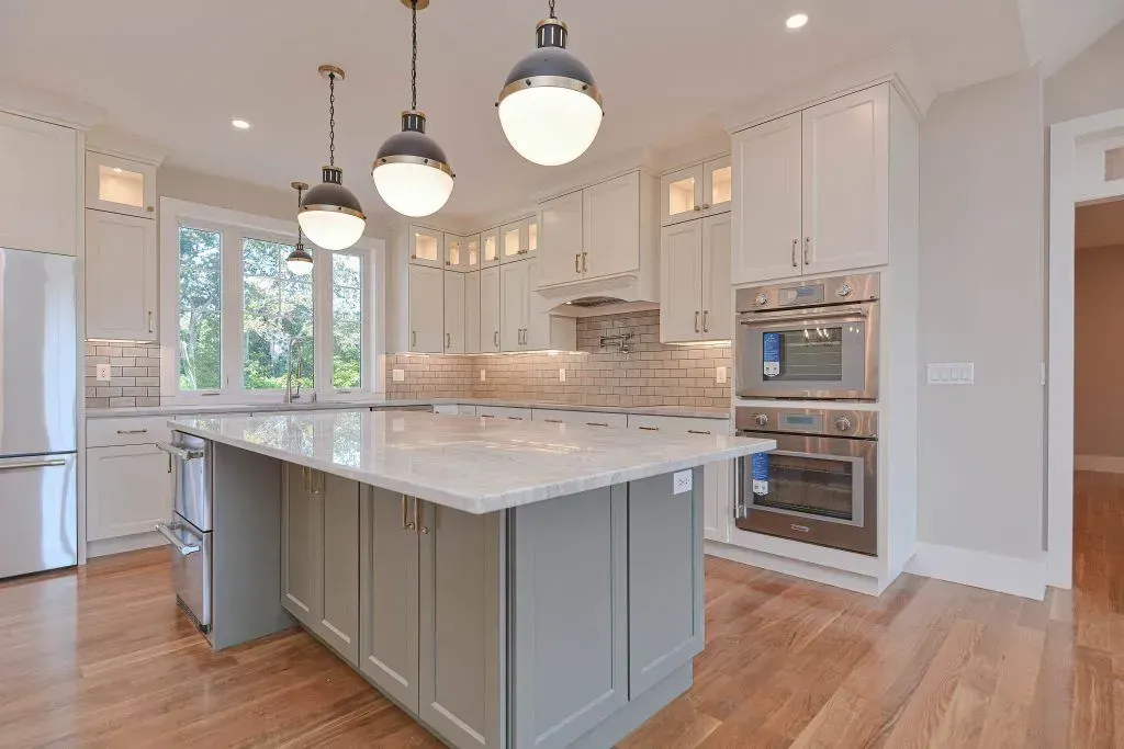 Spacious modern kitchen with white cabinetry, gray island, hardwood floors, and pendant lighting.