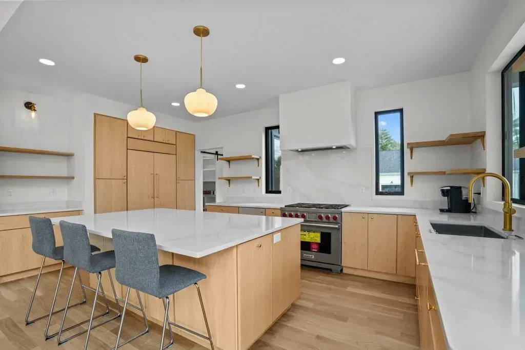 Modern kitchen with blonde wood cabinets, white countertops, and three pendant lights.