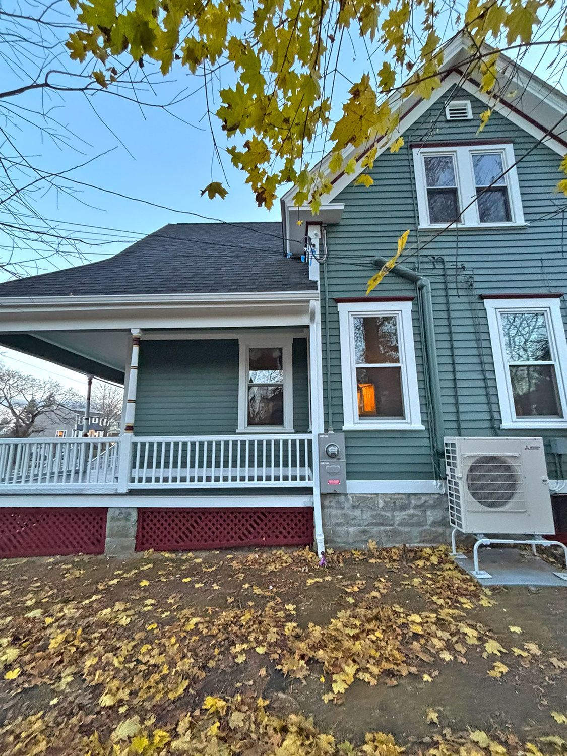 Green house with white trim, porch, and fallen leaves.