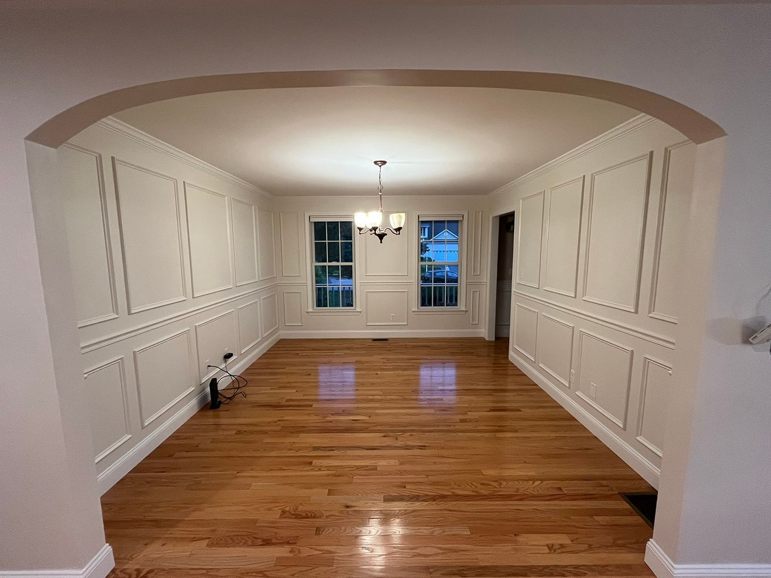 Empty dining room with wood floors and paneling on the walls. Archway in the foreground.