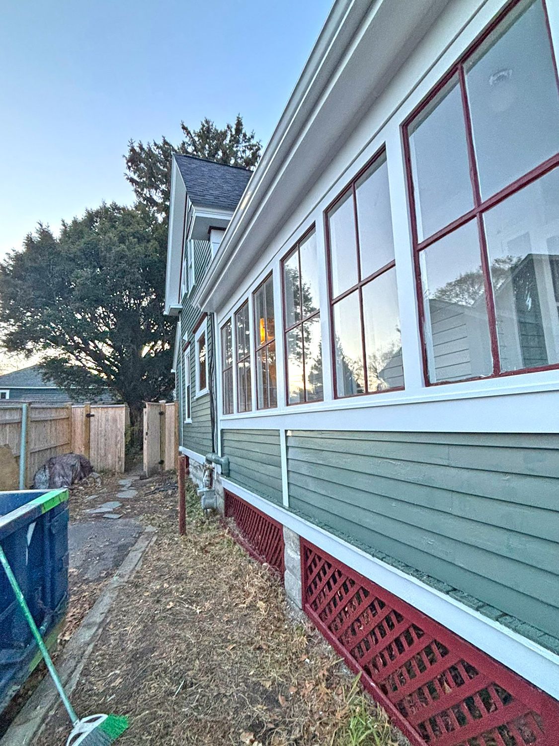 Side view of a house with many windows, red latticework, and green siding, set outdoors with a blue sky.