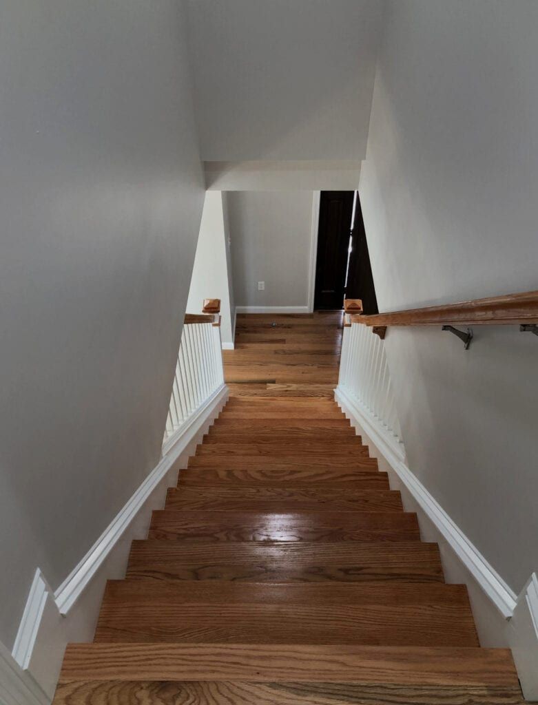 Wooden staircase with light gray walls and dark wooden handrails.