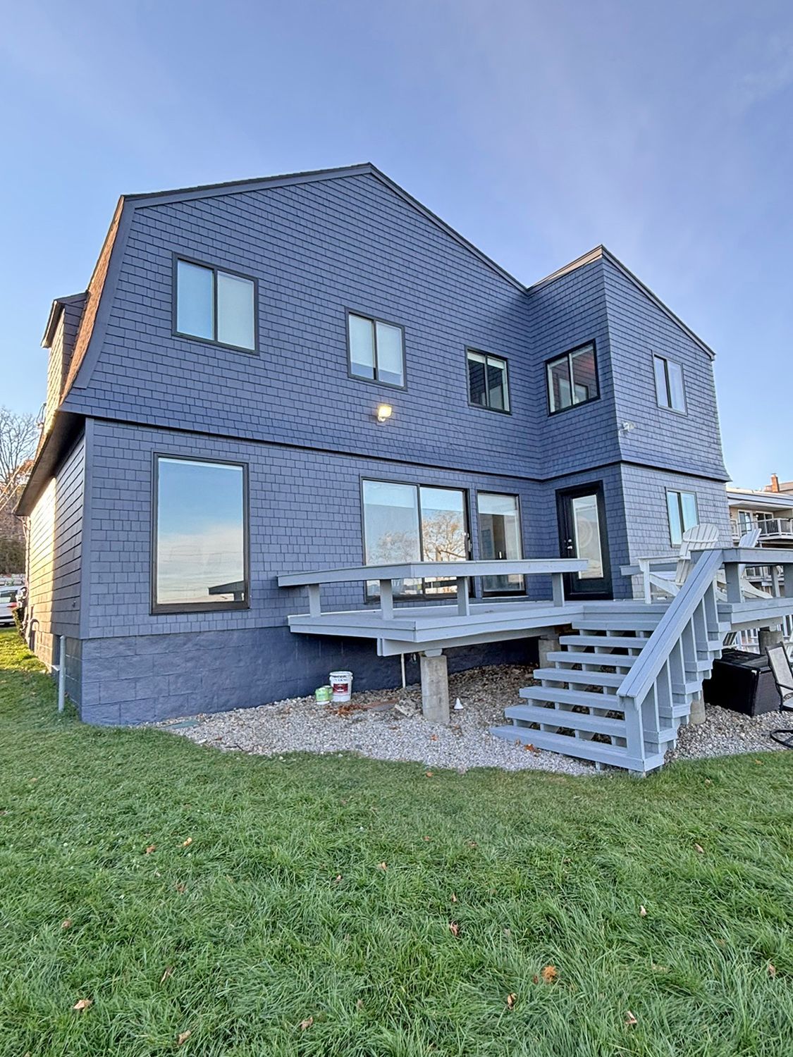 Blue-sided house with a gray deck and stairs leading down to a grassy yard under a blue sky.