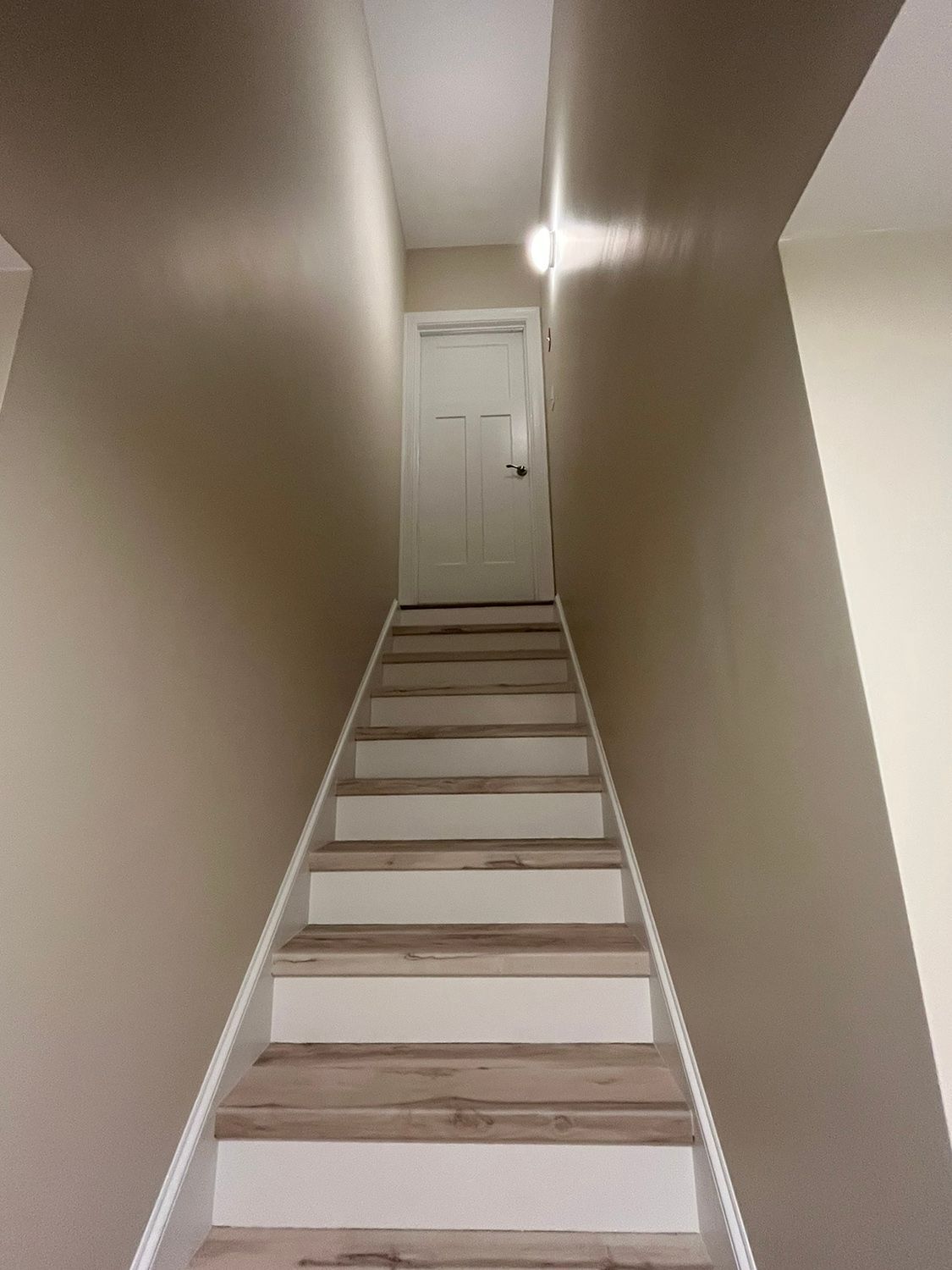 Staircase leading up to a white door. Beige walls, light-colored wooden steps with white risers.