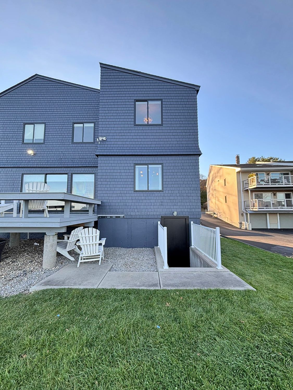 Blue-sided house with a deck, concrete patio, and a cellar door. Green lawn in the foreground.