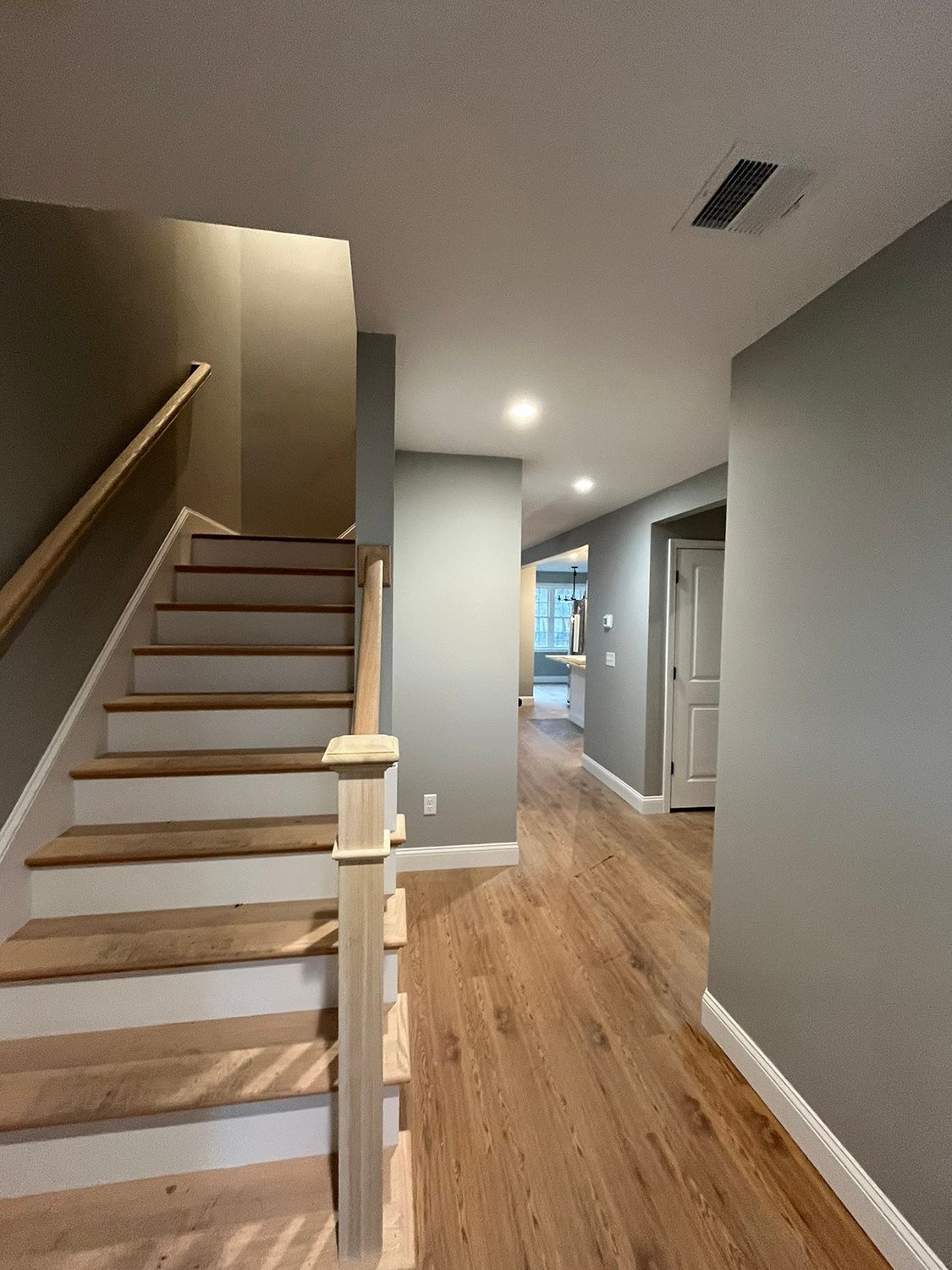 Staircase with wooden steps and a hallway with wood flooring and gray walls.