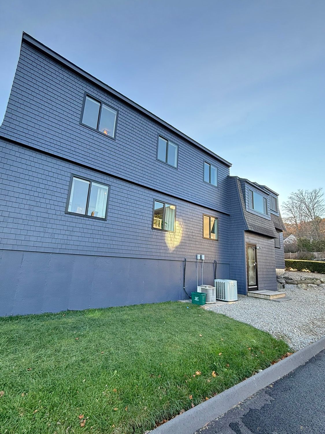 Blue-sided two-story building with multiple windows. Green lawn in foreground, gravel pathway, and clear sky in background.