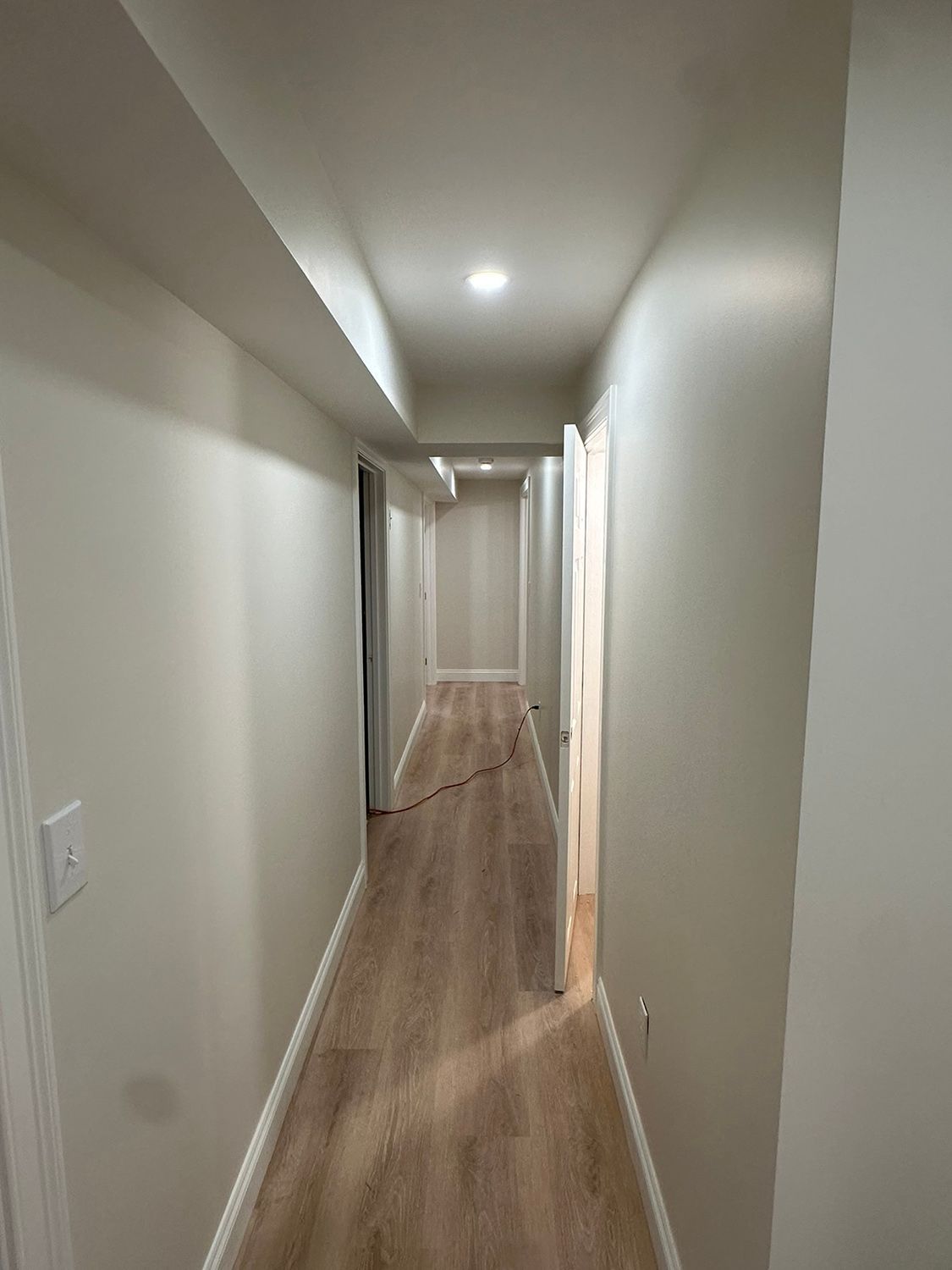 Long, narrow hallway with light-colored walls, wood-look flooring, and doorways leading off to the side.