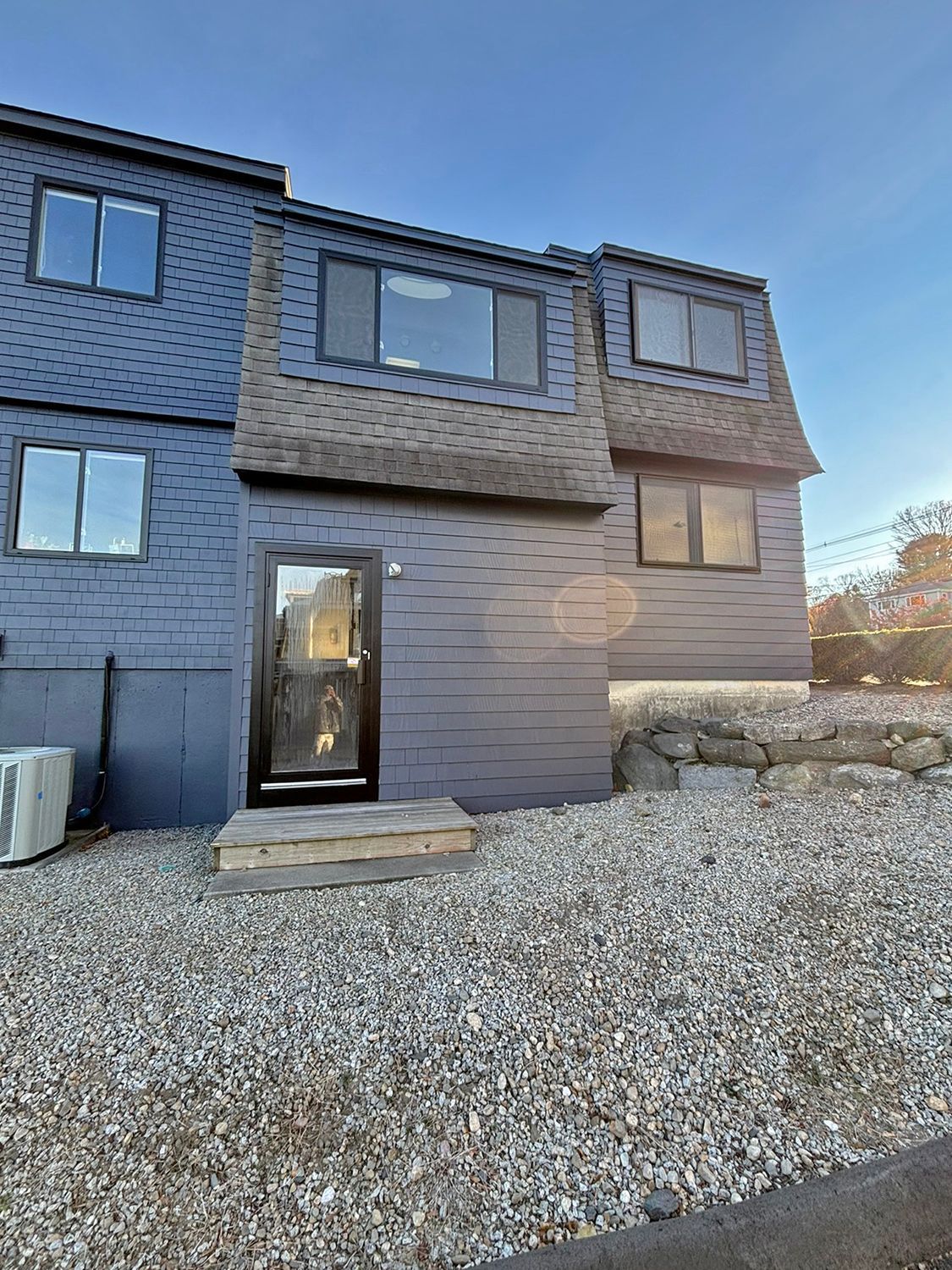 Blue townhouse with dark roof, small front steps, and gravel yard.