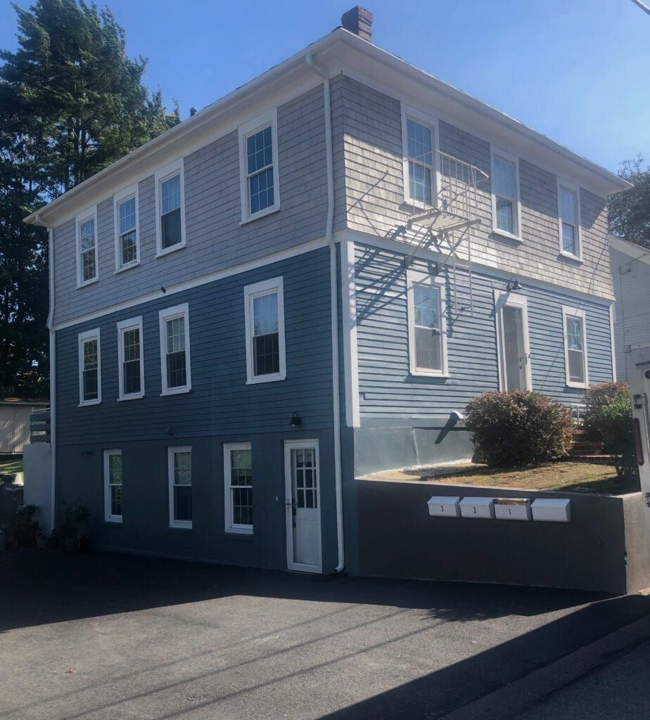 Two-story building with blue and gray siding, white-framed windows, and mailboxes.