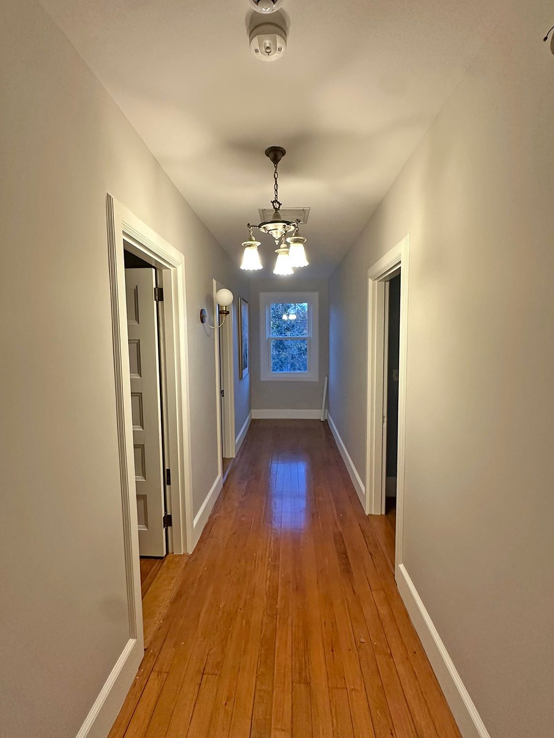 Narrow hallway with hardwood floor, doors on either side, and a light fixture.