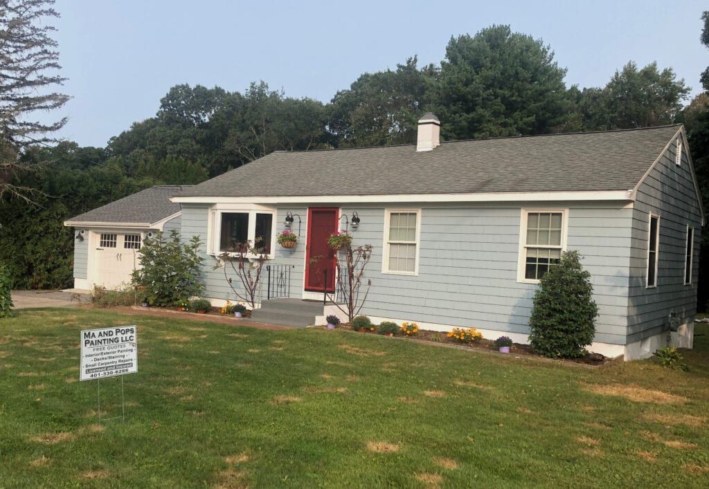 Light blue ranch house with a red door, white trim, and a gray shingle roof, on a grassy lawn.