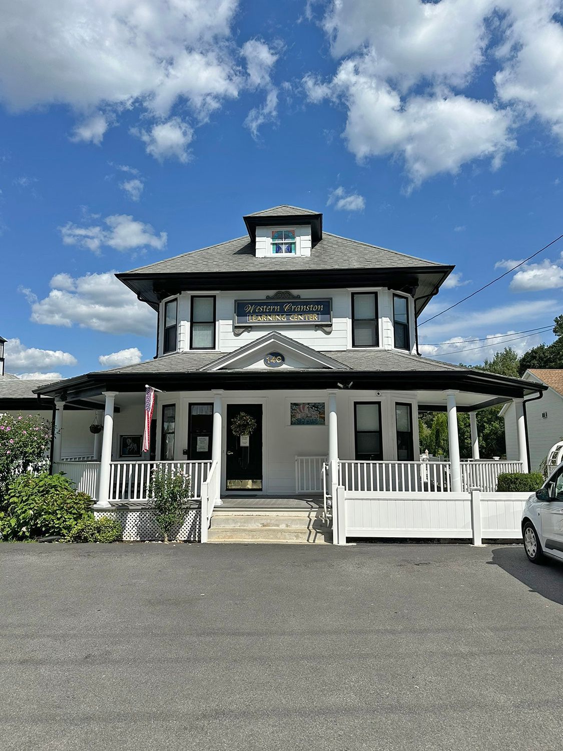 White two-story building with a porch, black door, and a sign that reads 