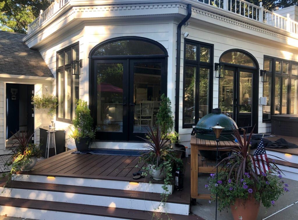 Exterior of a white house with black-framed windows, a dark wooden deck, and a green grill.