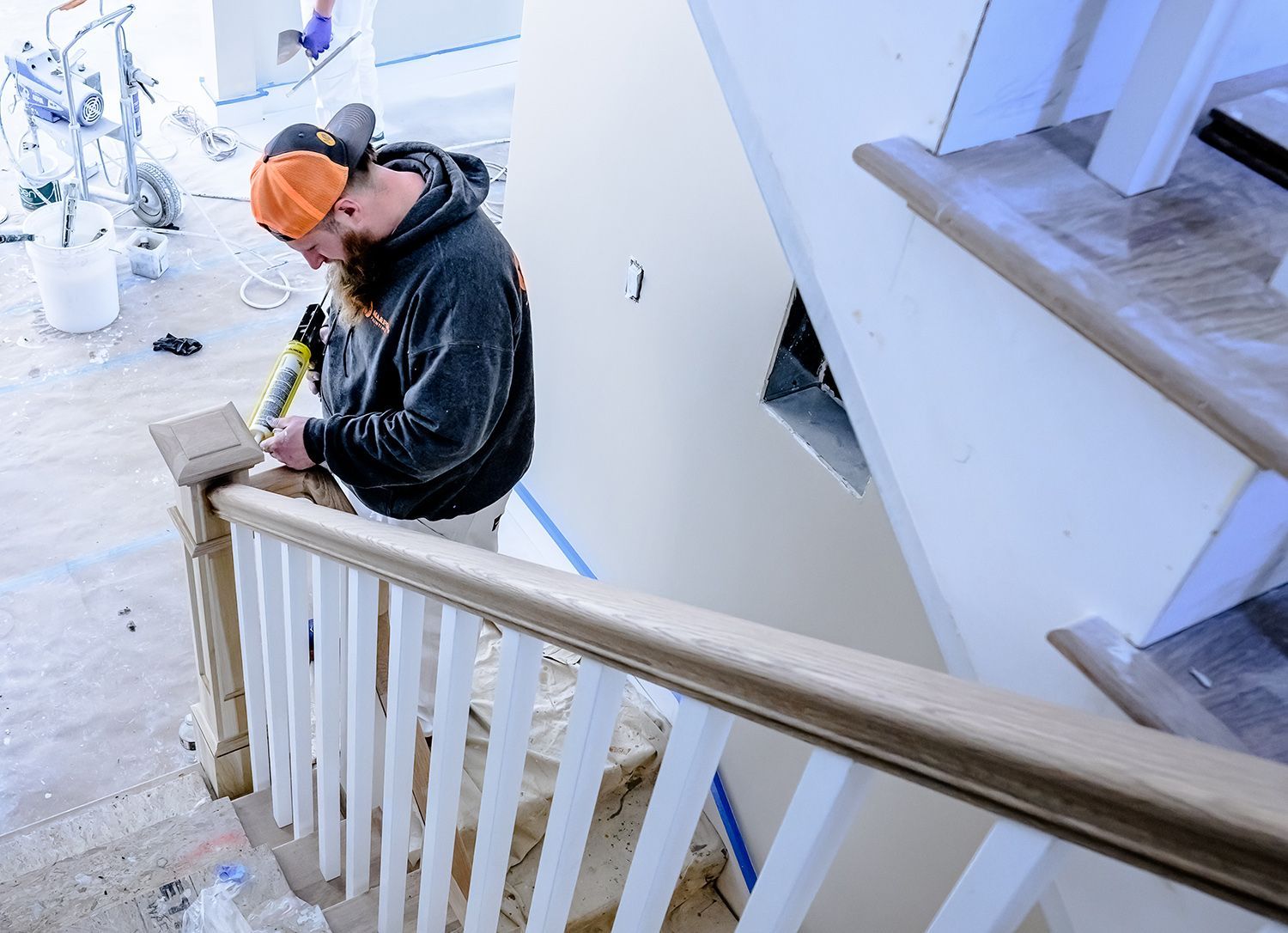 A person applies sealant to a wooden handrail on a staircase during home renovation.
