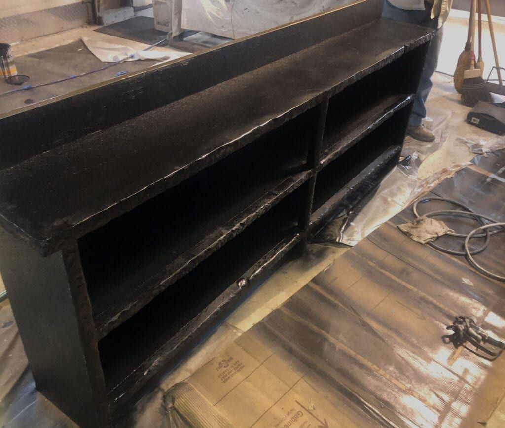 Black painted shelving unit on a tarped floor, possibly being painted.
