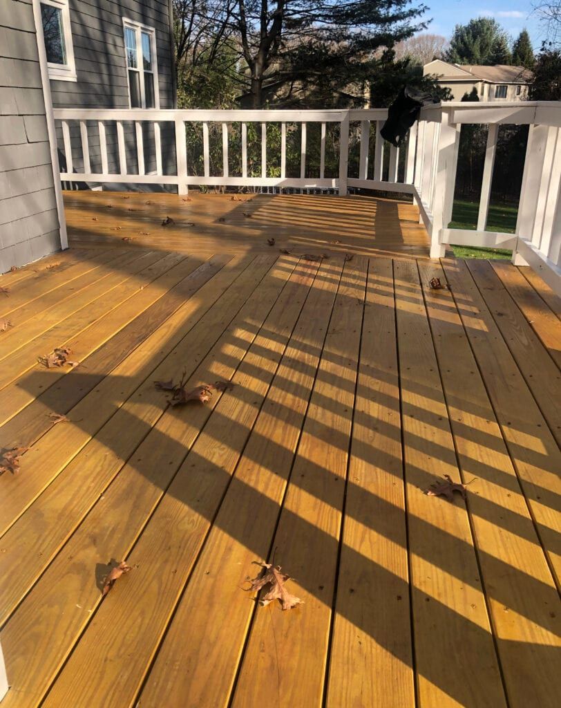 Wooden deck with white railing, covered in fallen leaves, casting long shadows.