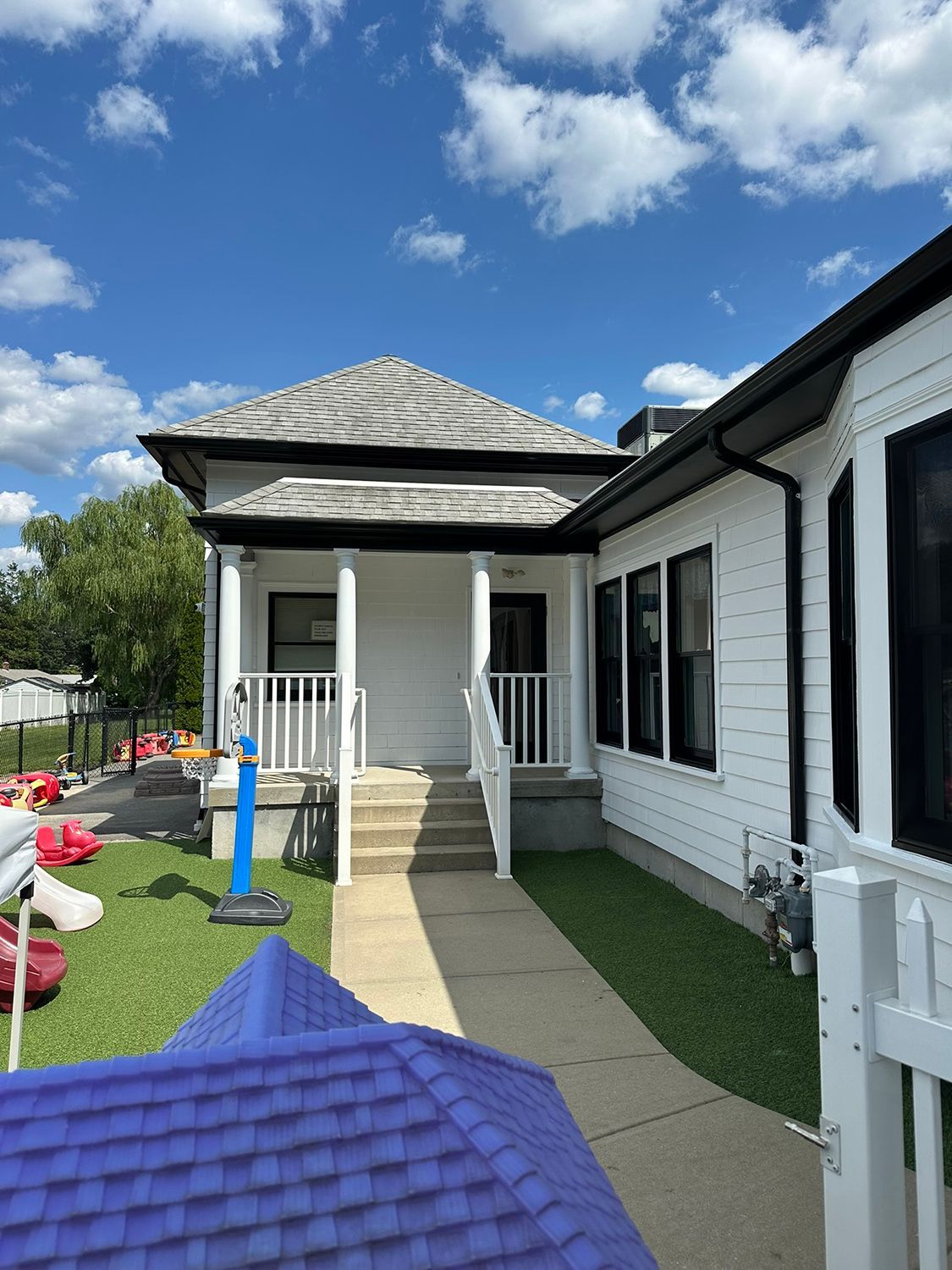 White building with black trim, concrete path to porch with stairs, blue sky.