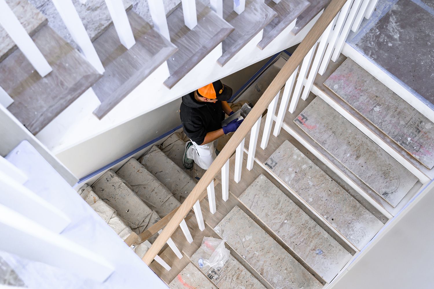 Person working on unfinished concrete stairs, wearing a hard hat, with white railing.