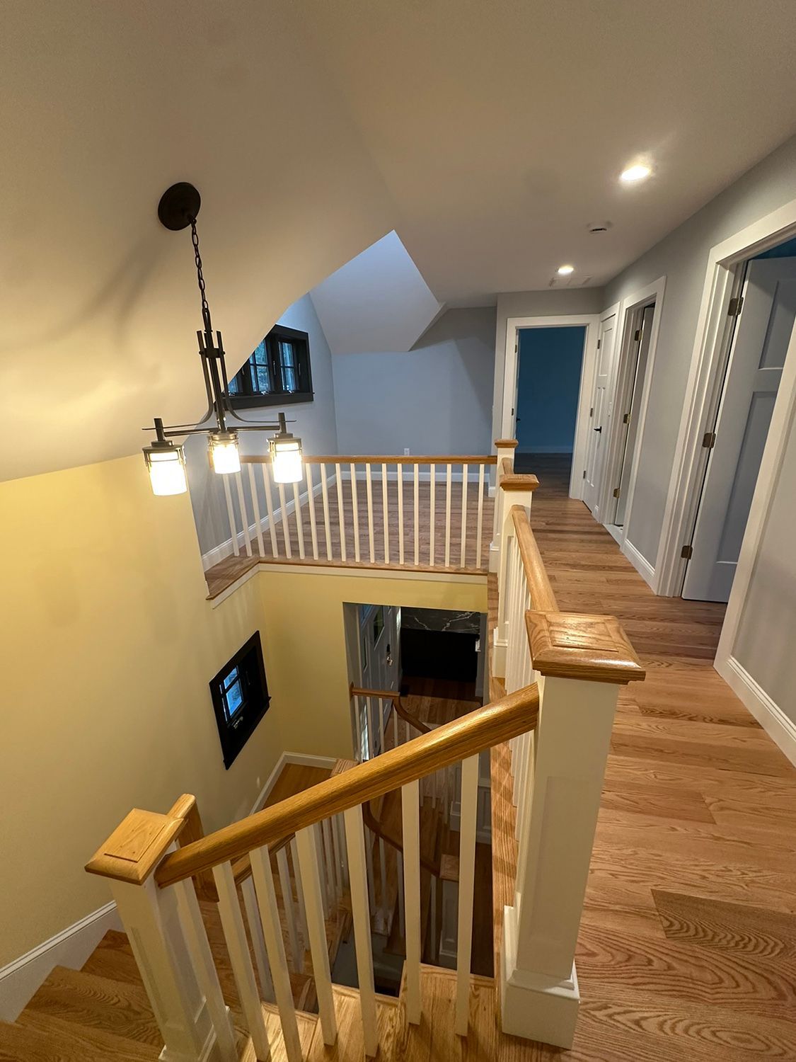 Staircase with wooden steps and railing, leading to a hallway with doors. Yellow and gray walls, chandelier.
