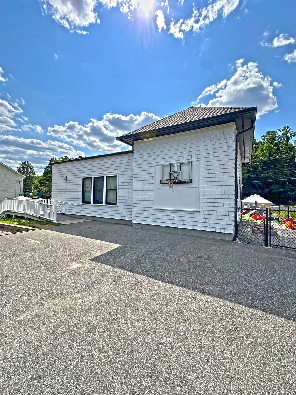 White building with shingled siding and a gravel driveway under a sunny sky.