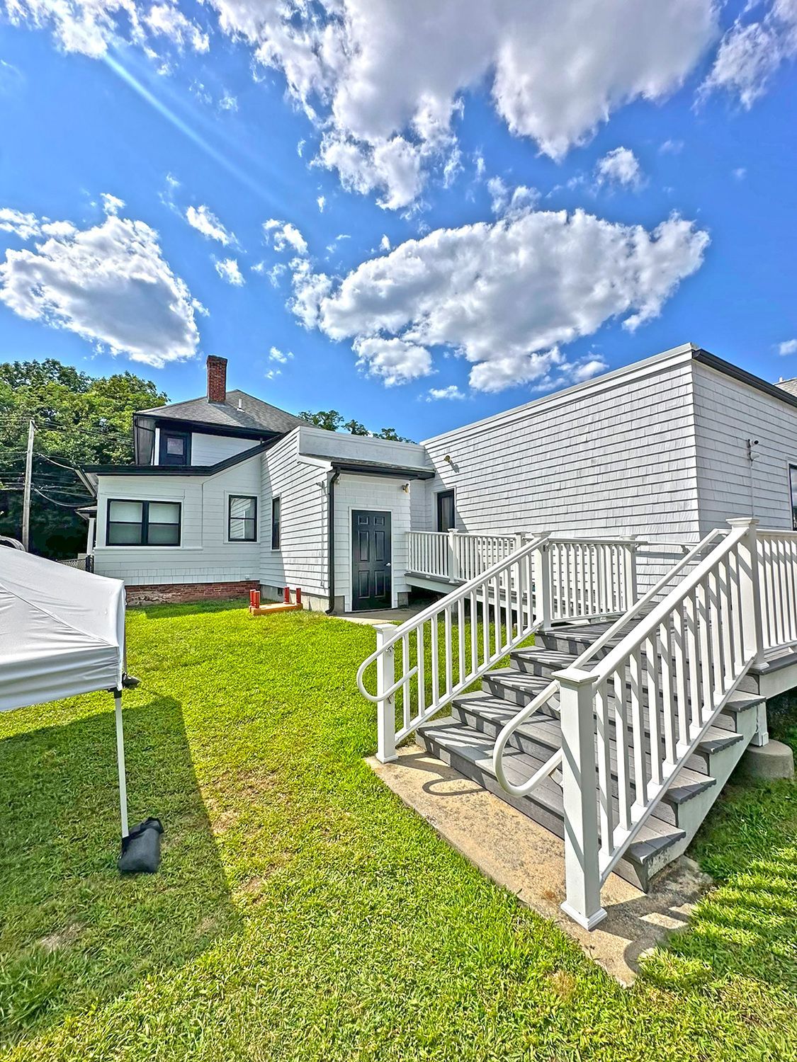 White buildings with stairs and a ramp on a grassy lawn under a partly cloudy sky.